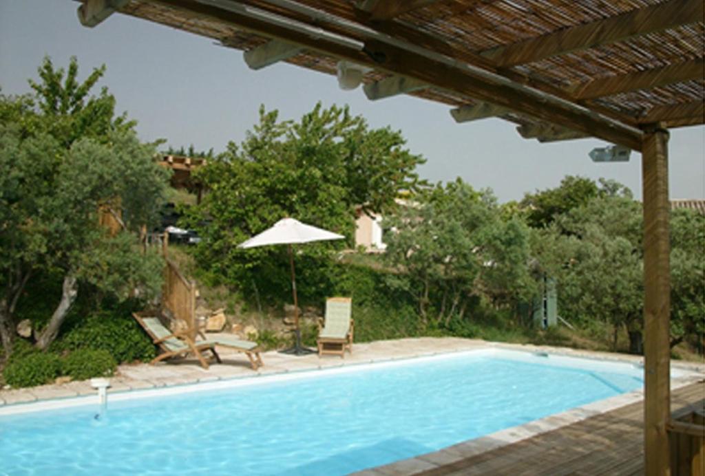 a swimming pool with an umbrella and chairs at The Neame House in Bédoin