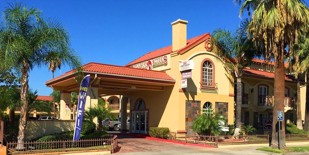 a yellow building with palm trees in front of it at Dynasty Suites Hotel in Riverside