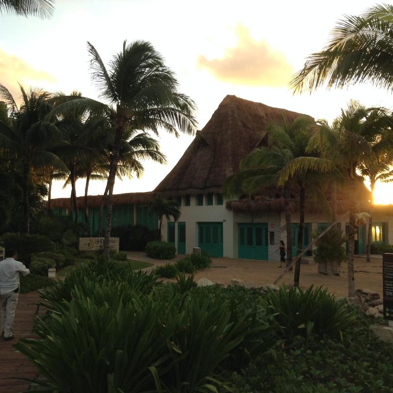 a house with a thatched roof and palm trees at Suites at Mayan Palace Vidanta Resort Riviera Maya in Playa del Carmen