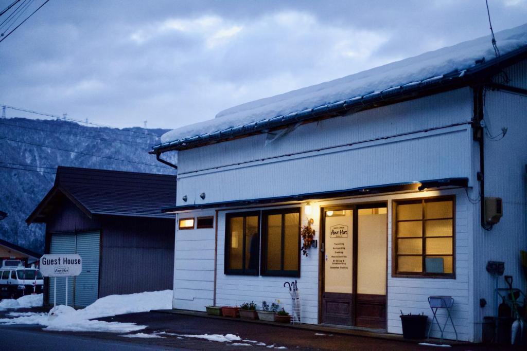 una pequeña casa blanca con nieve encima en Guesthouse AntHut, en Shirakawa