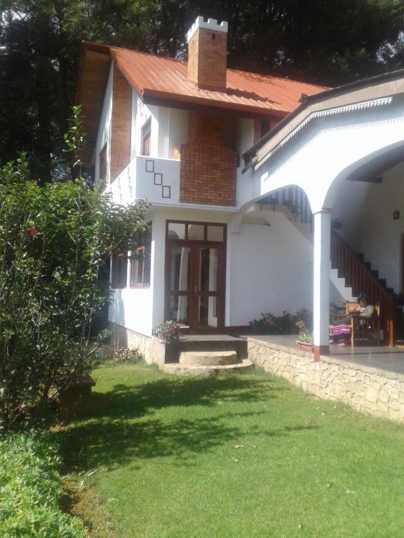 a white house with a red roof and a grass yard at Cecilia Cottage in Nuwara Eliya