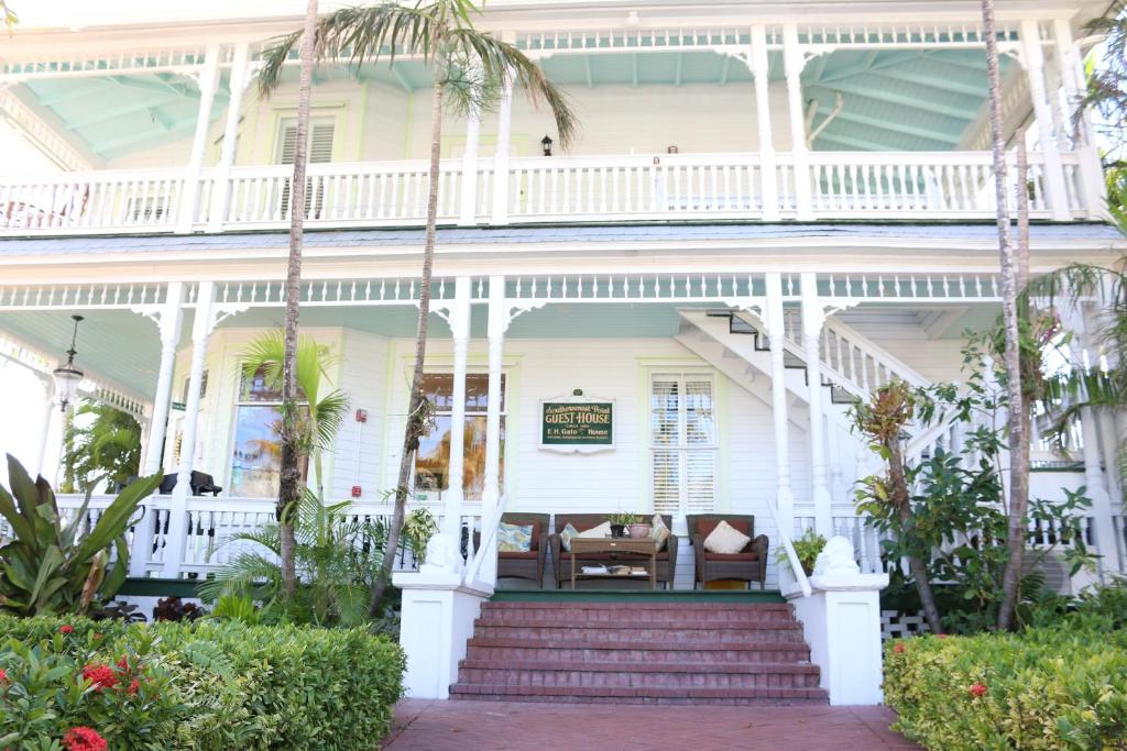 a white house with a porch with palm trees at Southernmost Point Guest House & Garden Bar in Key West