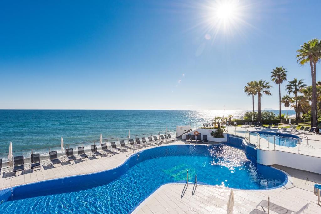 a pool with chairs and the ocean in the background at VIP Dominion Beach Estepona in Estepona