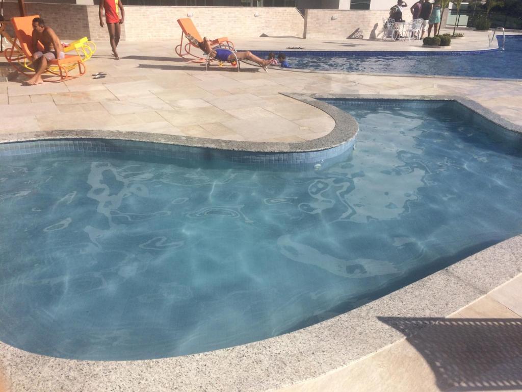 una piscina con gente sentada en sillas alrededor en LE BON VIVANT - LINDO APARTAMENTO PRAIA GRANDE, en Arraial do Cabo