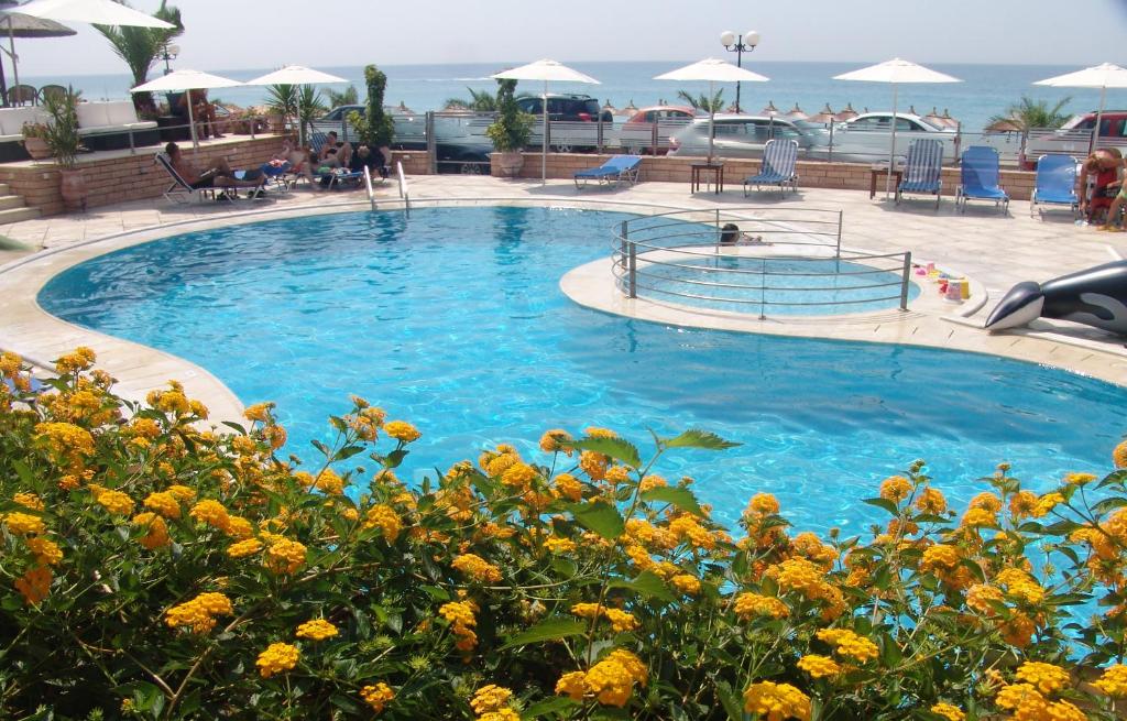 a large swimming pool with blue water and yellow flowers at Haris Hotel Apartments and Suites in Paralia Vrachou