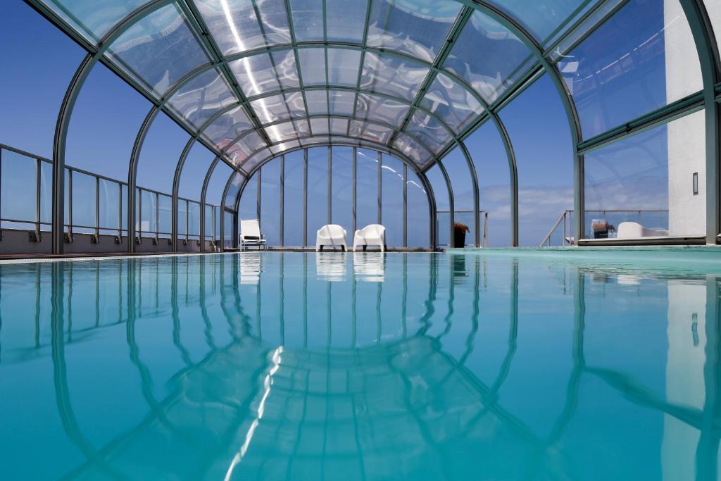 an indoor swimming pool with two white chairs in a building at Hotel Praia in Nazaré