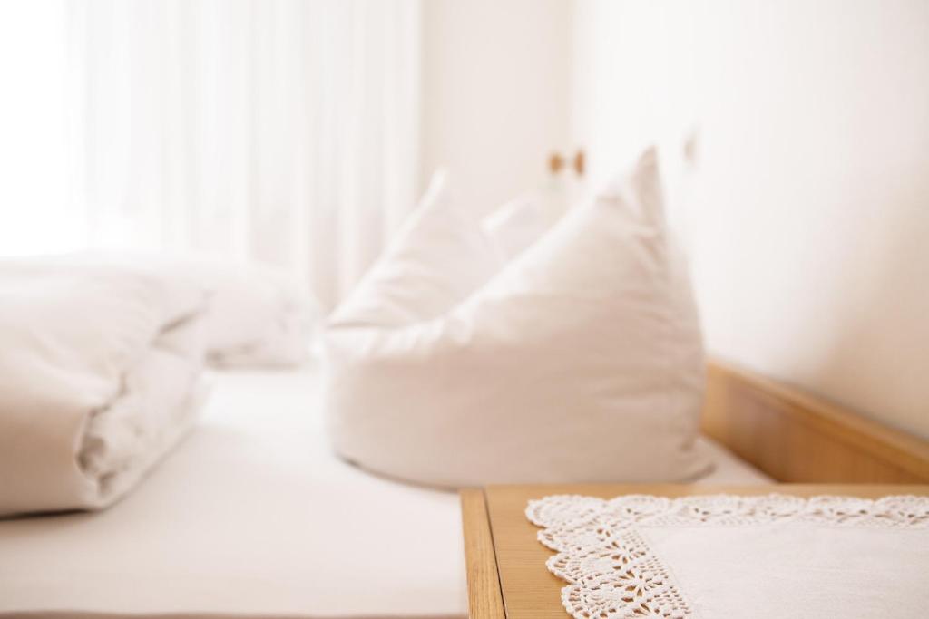 Una cama con almohadas blancas y una mesa con un libro. en Gästehaus Meusburger en Bezau