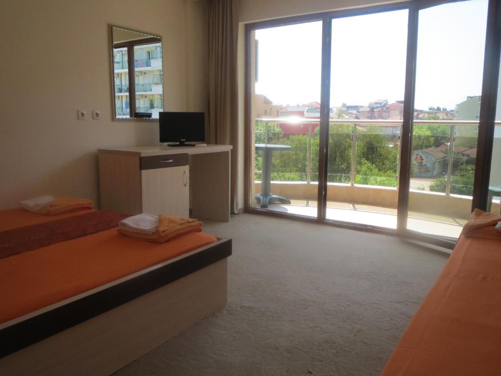 a room with two beds and a television and a balcony at Family Hotel Golden Lion in Primorsko