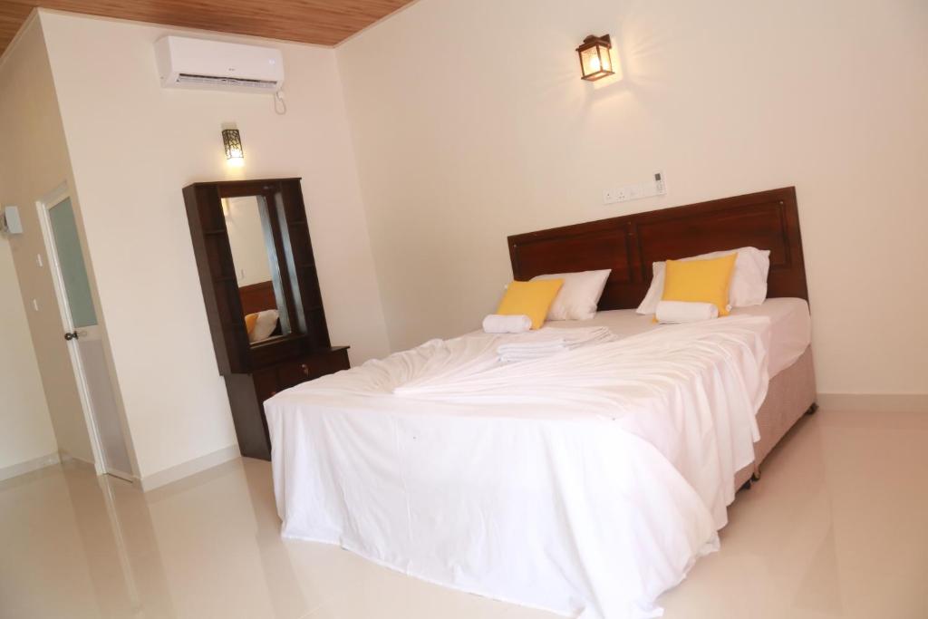 a bedroom with a bed with white sheets and yellow pillows at Serene Beach Hotel in Dickwella