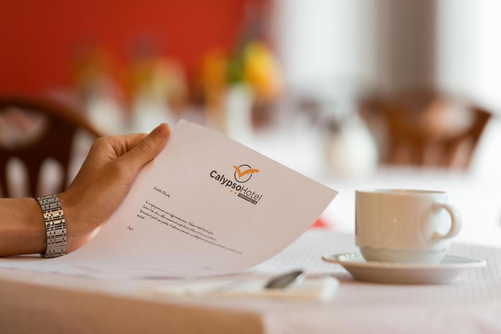 a person holding a piece of paper with a cup of coffee at Hotel Calypso in Ventimiglia