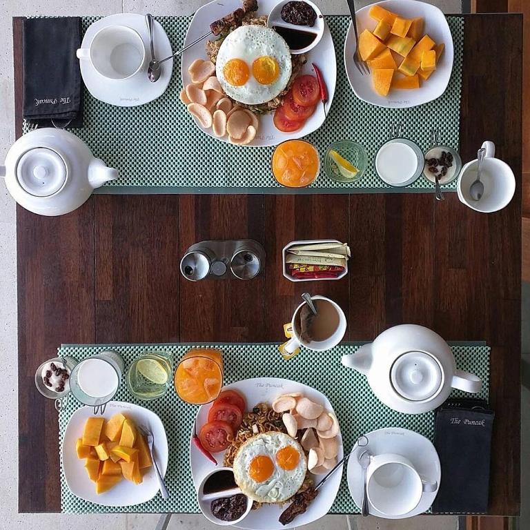 a table topped with plates of food with eggs and fruit at The Puncak Lombok in Senggigi