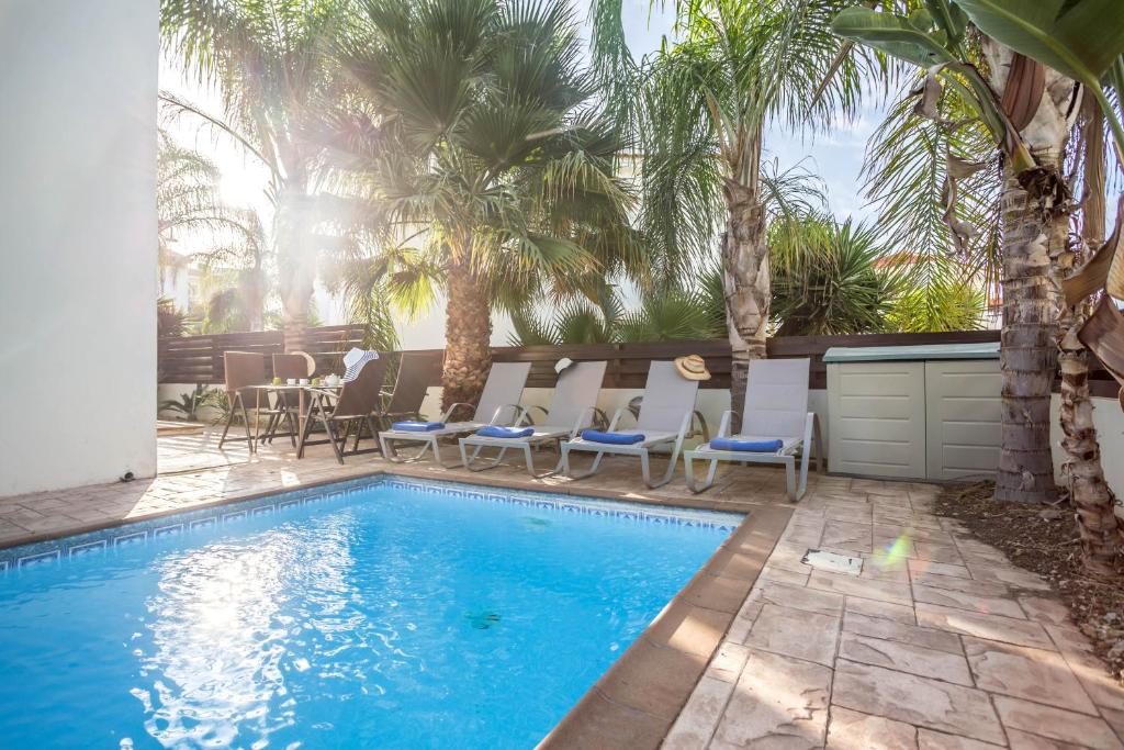 a swimming pool with chairs and a table and palm trees at Villa Costas in Protaras