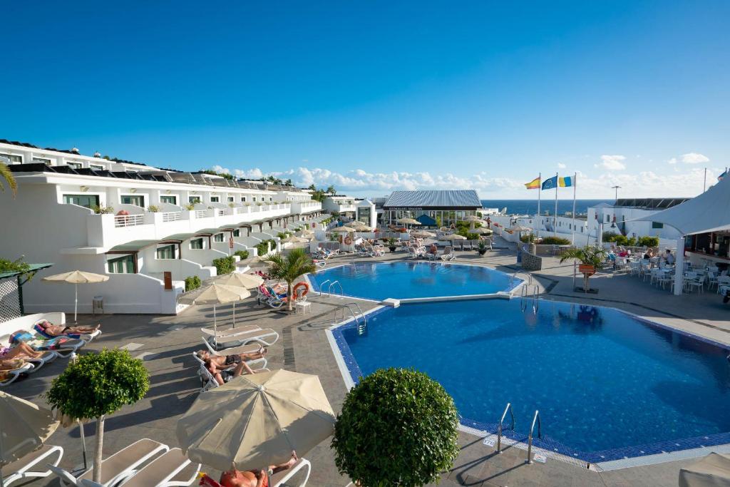 un hotel con una piscina con sillas y sombrillas en Relaxia Lanzaplaya, en Puerto del Carmen