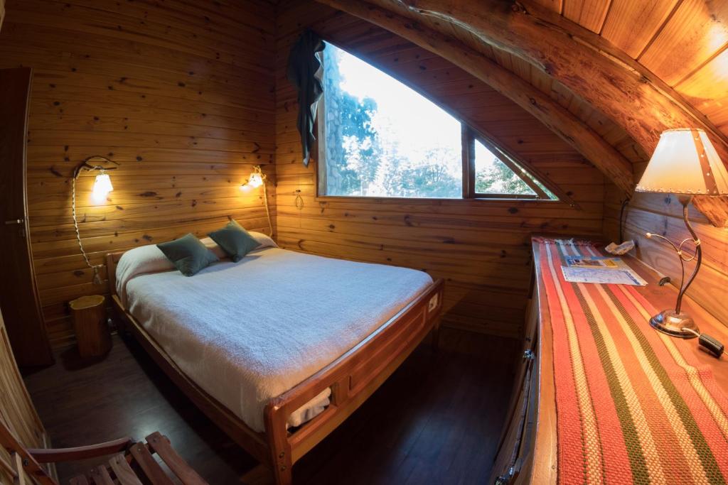 una camera da letto in una baita di tronchi con un letto e una finestra di El Aleph a Villa La Angostura