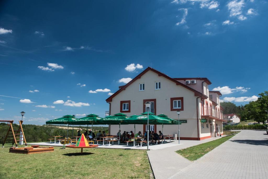 un edificio con una mesa con sombrillas verdes y un parque infantil en Penzion U Výra, en Výrovice