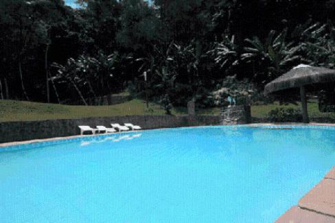 una gran piscina azul con 2 tumbonas en Pousada A Marca do Faraó, en Cachoeiras de Macacu