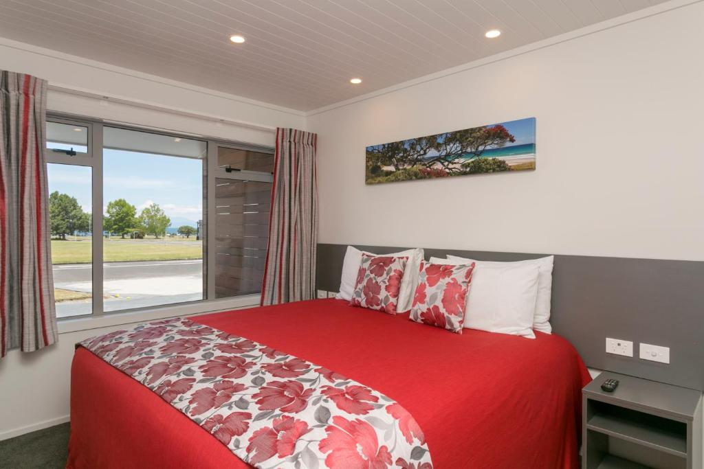 a bedroom with a red bed and a window at eMotel in Taupo