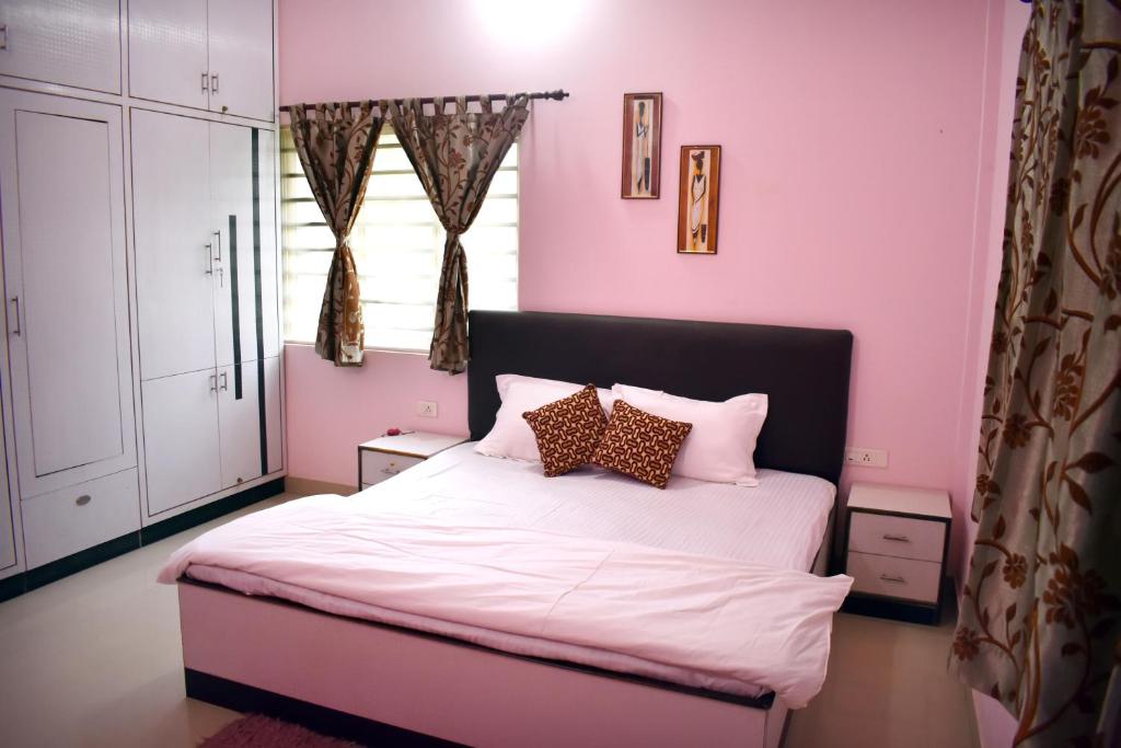 ein rosafarbenes Schlafzimmer mit einem Bett mit weißer Bettwäsche und Kissen in der Unterkunft Tranquil Hospitality in Bhubaneshwar