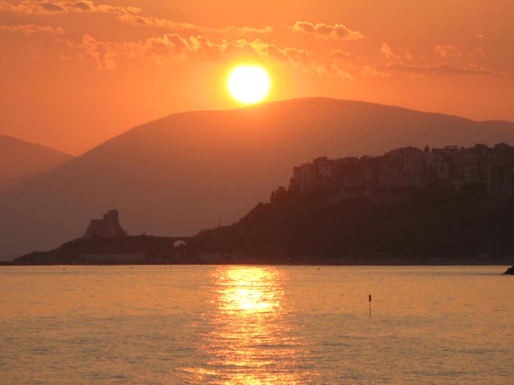 einen Sonnenuntergang über dem Wasser mit einer Stadt im Hintergrund in der Unterkunft Hotel Club Torre Capovento in Sperlonga