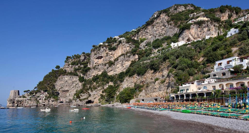 a beach with chairs and buildings and a mountain at Hotel Pupetto in Positano