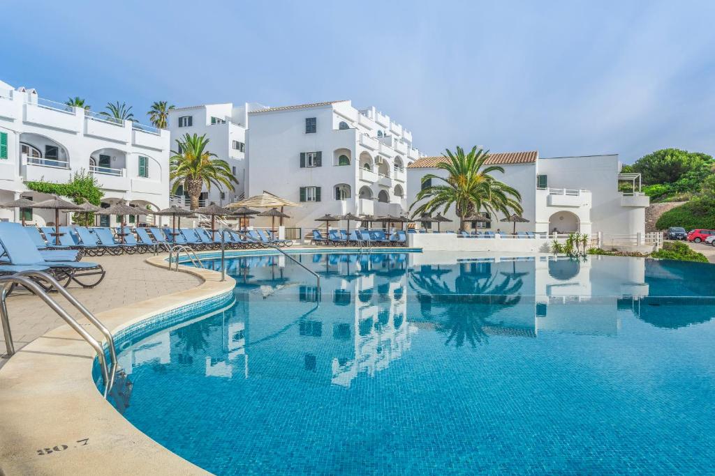 - une piscine d'eau bleue en face des bâtiments dans l'établissement White Sands Beach Club, à Arenal d'en Castell