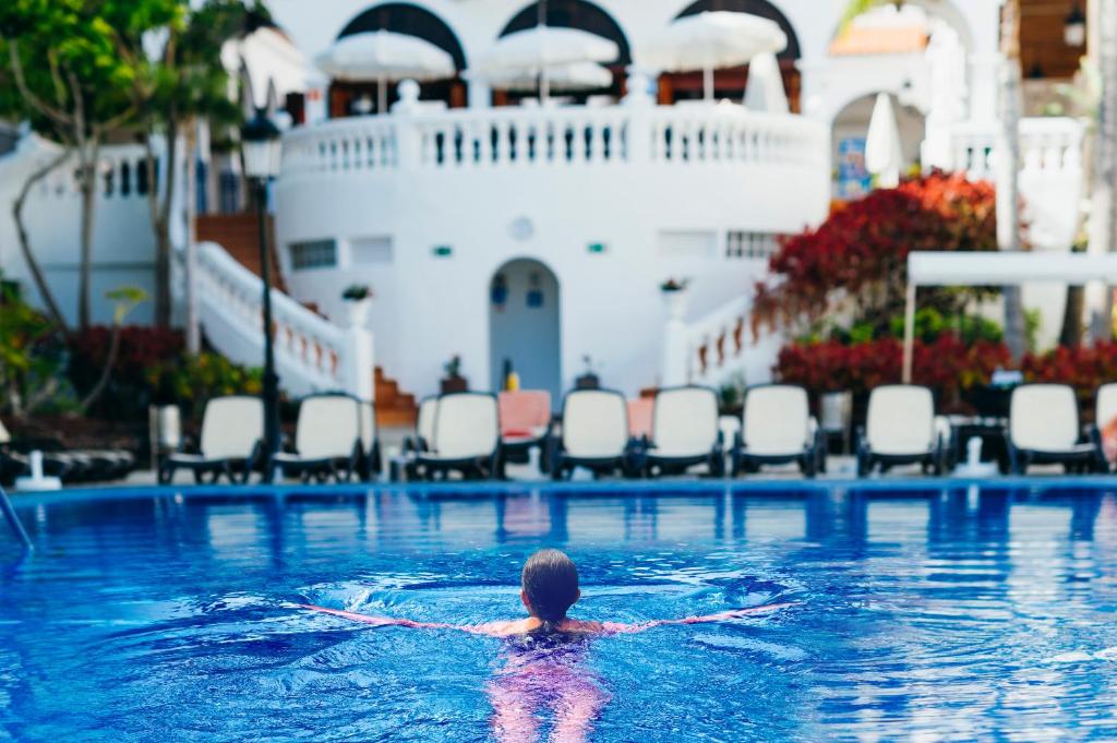 a person in a swimming pool with a cruise ship at Beverly Hills Heights - Excel Hotels & Resorts in Los Cristianos