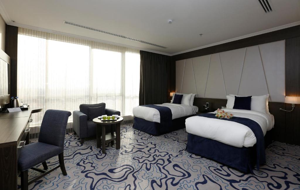 a hotel room with two beds and a desk at Swiss Flora Royal Hotel Riyadh in Riyadh