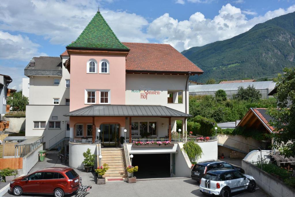 una casa rosa con techo verde y 2 coches aparcados en Hotel Tanja-Sonnenhof en Laces