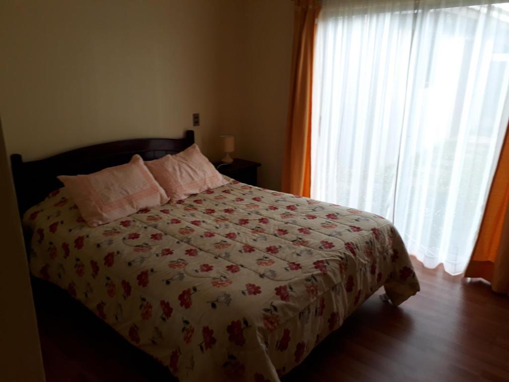 a bedroom with a bed with a flowered blanket and a window at Casa Jardines del Mar, Puerto Montt in Puerto Montt