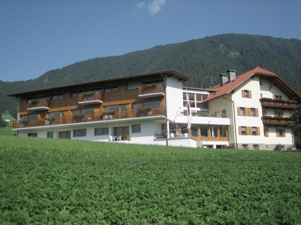 un grand bâtiment sur une colline avec un champ verdoyant dans l'établissement Garni - Appartement Neumairhof, à Rasun di Sopra