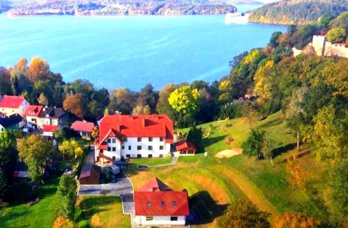 a house with a red roof on a hill next to the water at Hotel Kasztelan in Dobczyce