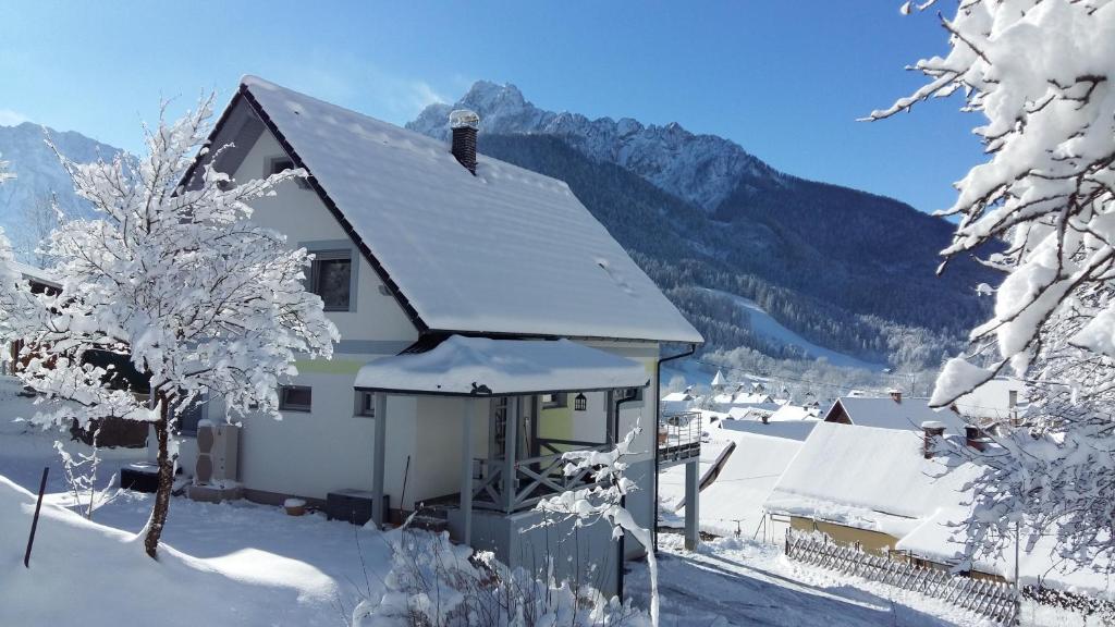 une maison recouverte de neige avec des montagnes en arrière-plan dans l'établissement Apartment Leposa, à Kranjska Gora