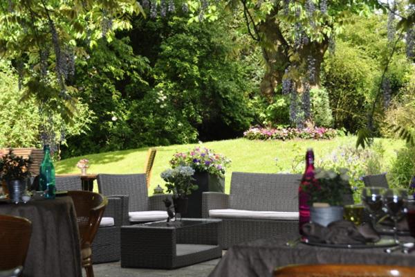 an outdoor patio with tables and chairs and a garden at Hôtel Beatus in Cambrai