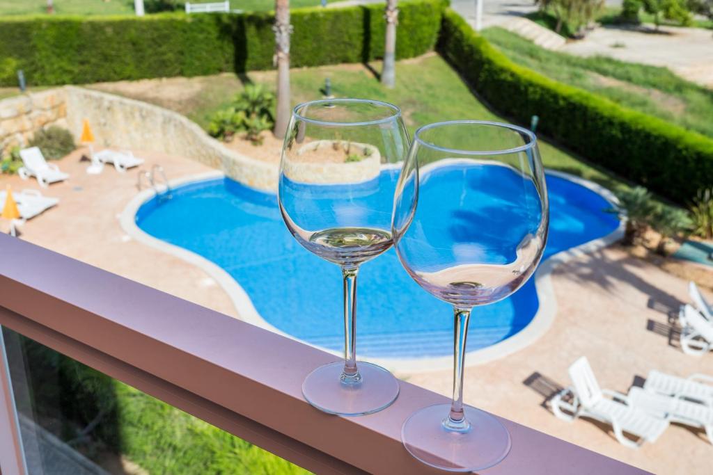 dois copos de vinho sentados numa saliência ao lado de uma piscina em Litoralmar Beach Apartment em Portimão