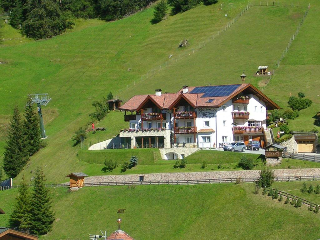 a large house on top of a green hill at Garni La Tambra in Selva di Val Gardena