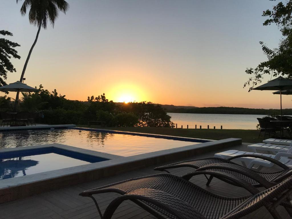 a pool with chairs and a sunset in the background at Pousada Porto Manguaba in Japaratinga