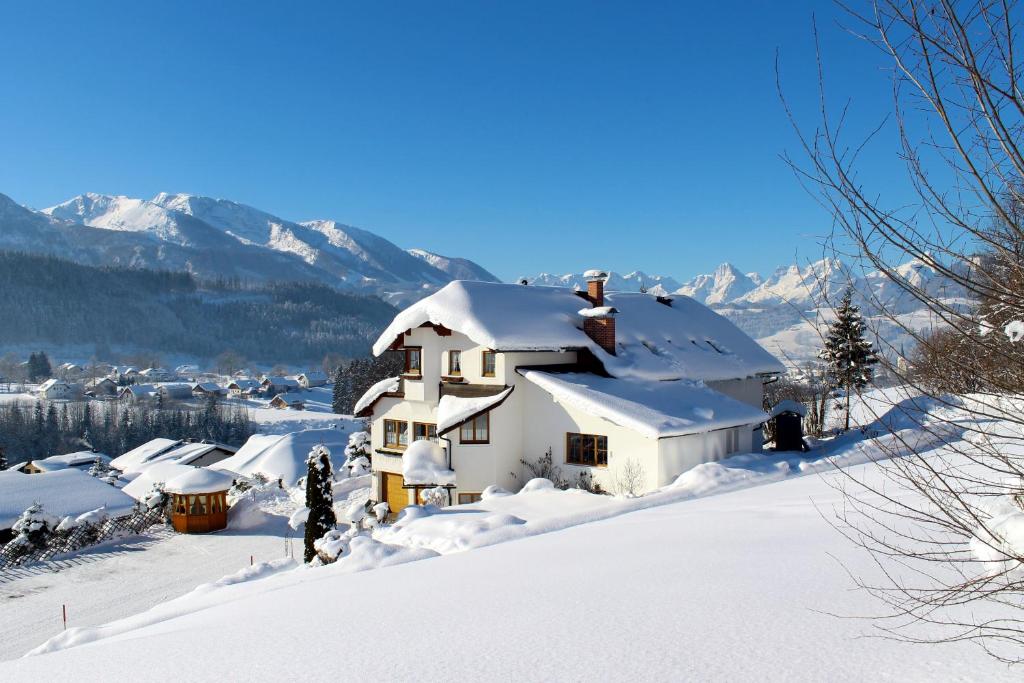 une maison recouverte de neige avec des montagnes en arrière-plan dans l'établissement Haus Löger Apartments Pyhrn Priel, à Windischgarsten