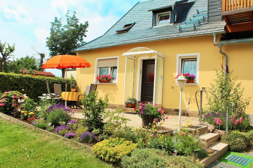 a yellow house with a garden with flowers and an umbrella at Ferienwohnung Gramalla in Bad Steben