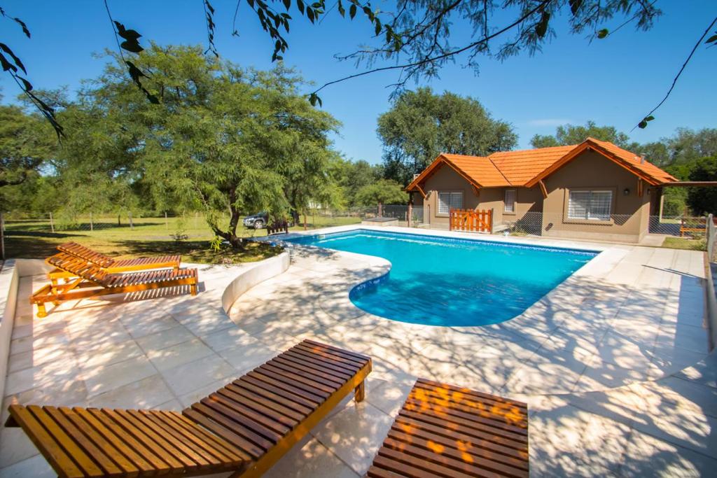una piscina con bancos y una casa en El Refugio Casas de Campo en Villa General Belgrano
