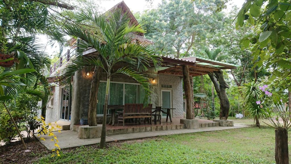 a house with a porch with a table and palm trees at Baantantara in Suan Phung