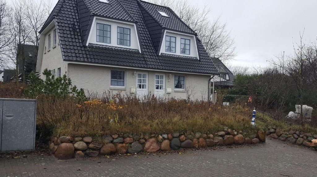 a house with a gambrel roof and a rock wall in front at Wohnung-Wattseite in Munkmarsch