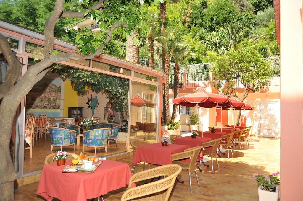 un restaurant avec des tables rouges, des chaises et des arbres dans l'établissement Hotel Menton Riviera, à Menton