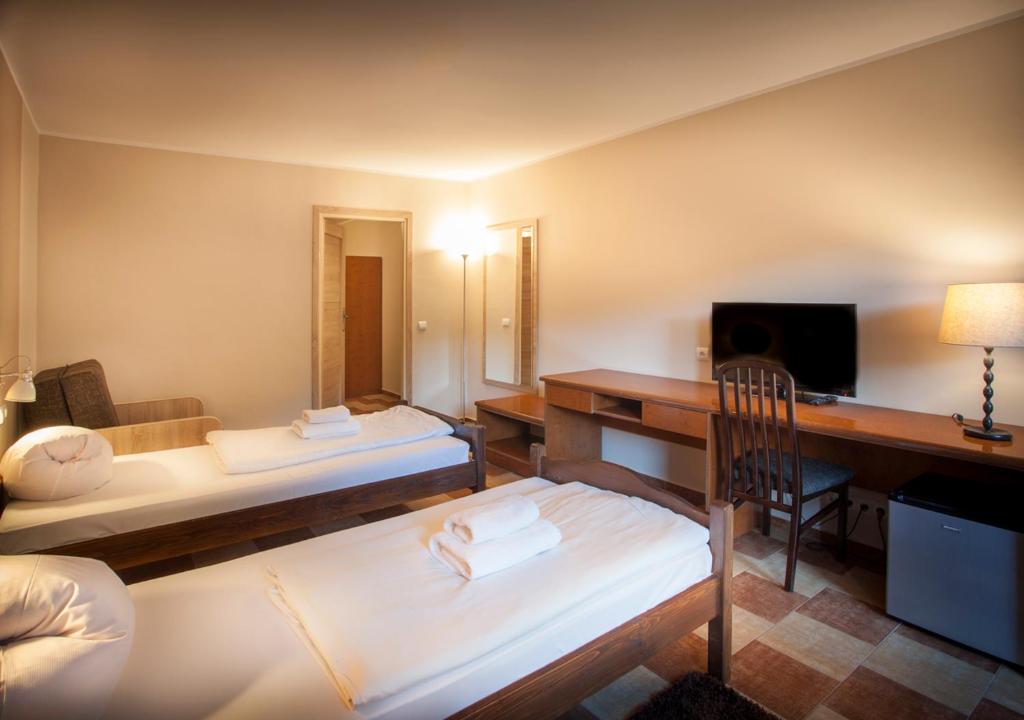 Two single beds in warm-lit hotel room with desk, TV, and folded towels