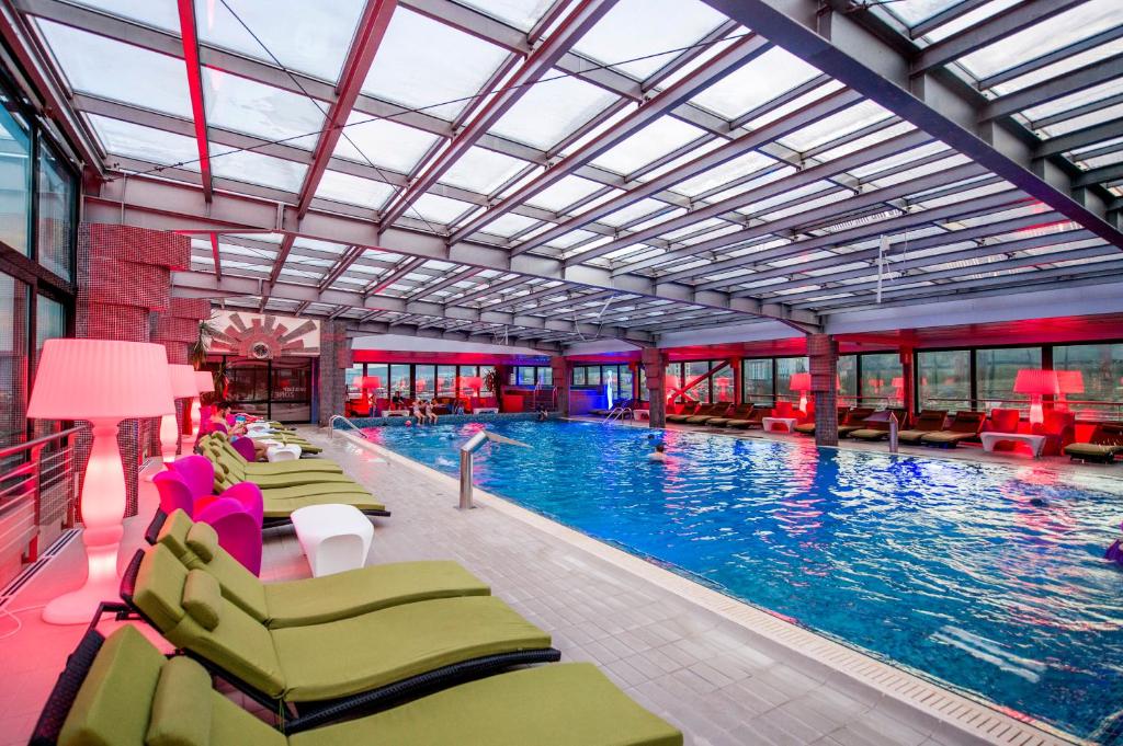 a large swimming pool with chairs and a person in the water at Business Hotel Conference Center & Spa in Târgu-Mureş