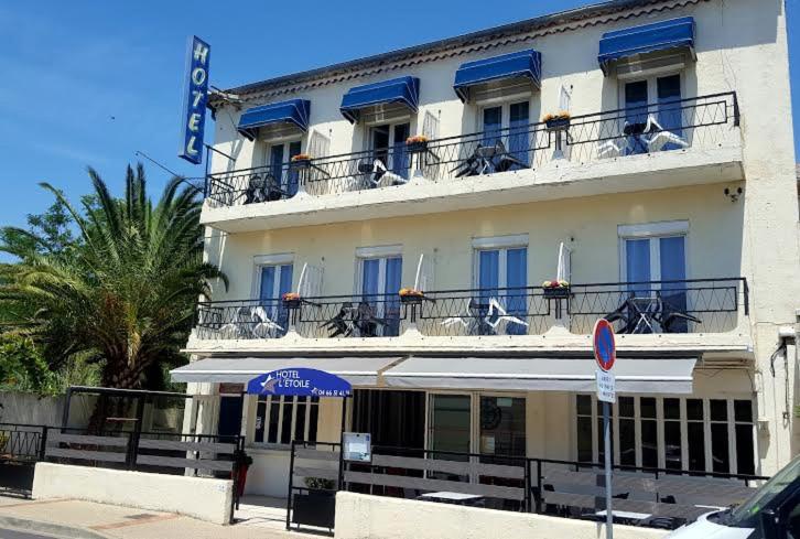 a large white building with blue windows and balconies at Hôtel l'Etoile in Le Grau-du-Roi