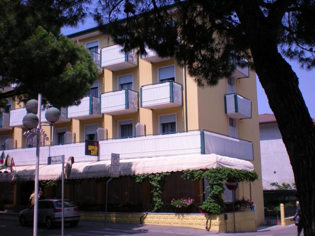 um edifício amarelo com varandas brancas e uma árvore em Hotel Portofino em Caorle