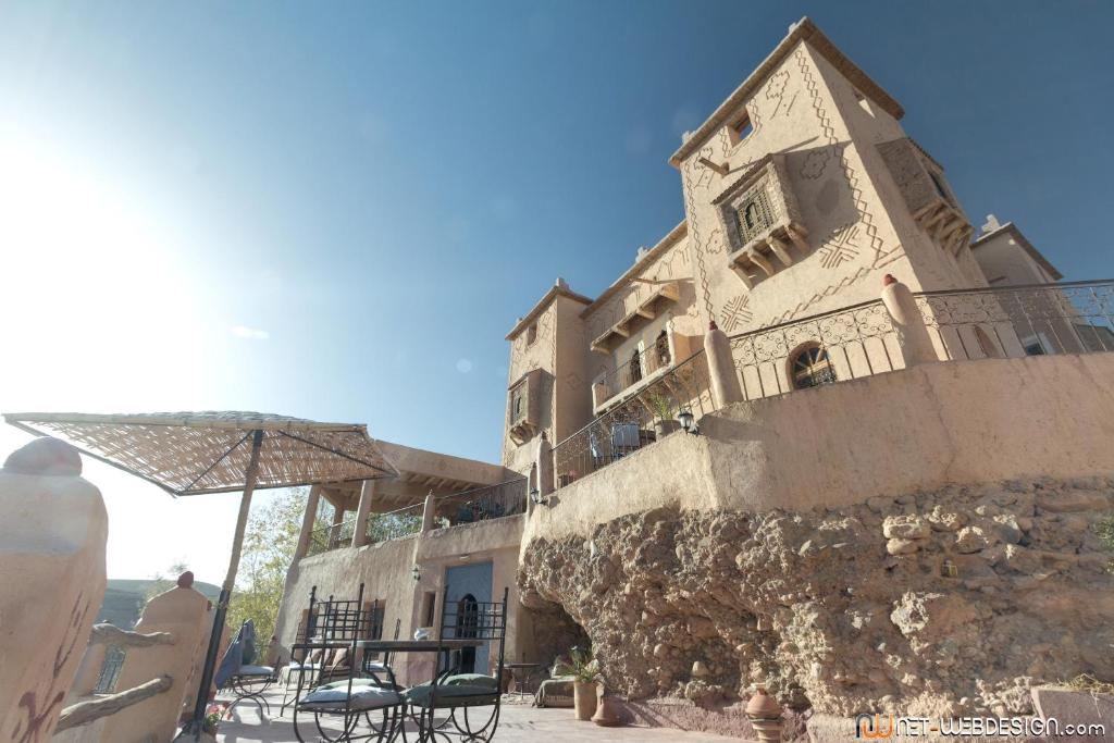 ein Gebäude mit einem Tisch, Stühlen und einem Sonnenschirm in der Unterkunft Kasbah Agoulzi in El-Kelâa M’Gouna