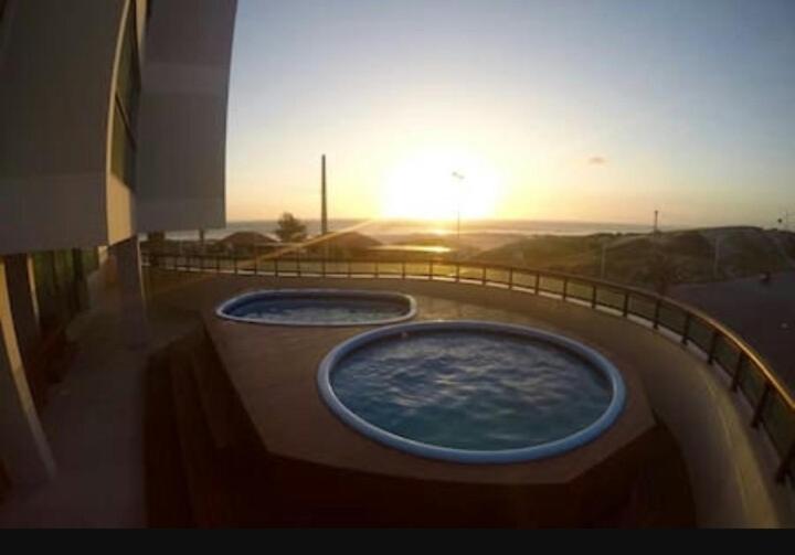 Dos bañeras de hidromasaje en un edificio con la puesta de sol en el fondo en Sophia 1, en Arraial do Cabo