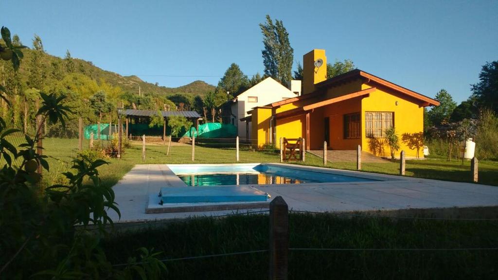 a swimming pool in front of a yellow house at Cabañas Lomas de Calamuchita in Santa Rosa de Calamuchita