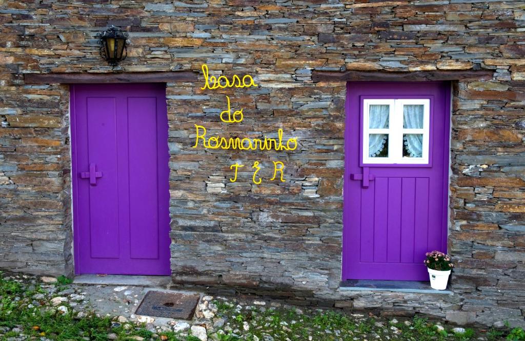 twee paarse deuren aan de zijkant van een bakstenen gebouw bij Piódão Casa do Rosmaninho TER in Coja